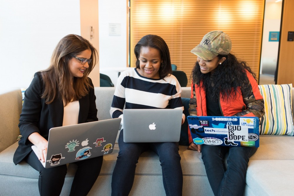 Drei Frauen sitzen zusammen auf einem Sofa und arbeiten auf ihren Laptops.