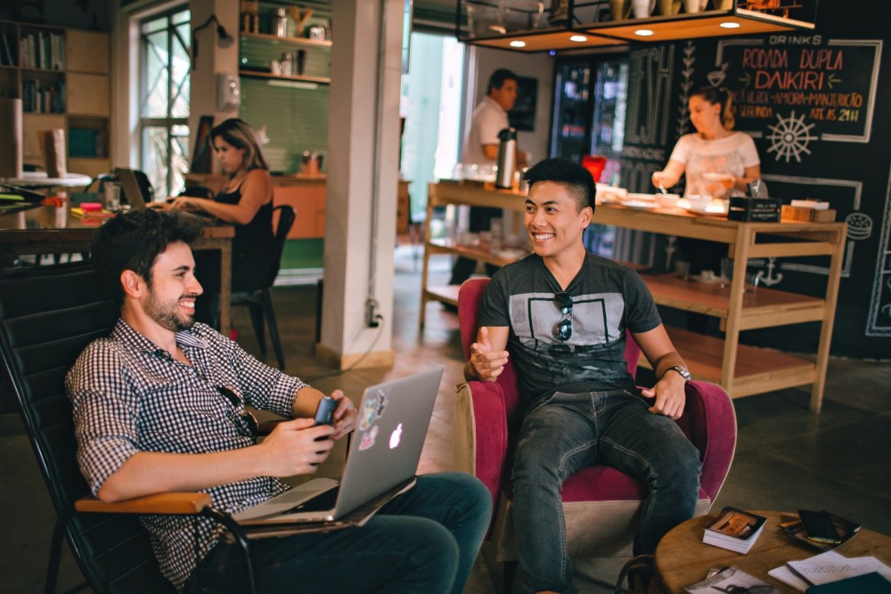 Zwei Männer sitzen in einem Co-Workingspace zusammen und arbeiten an einem Laptop.