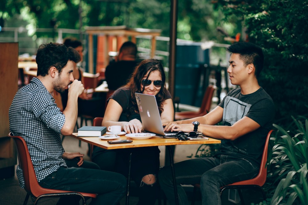 Drei junge Menschen sitzen zusammen in einem Cafe und arbeiten an einem Laptop.