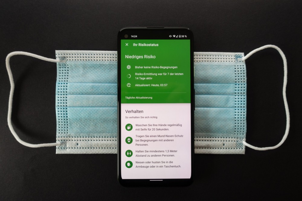 Ein Smartphone zeigt die Corona-Warnapp und liegt auf einer Mund-Nasen-Maske.