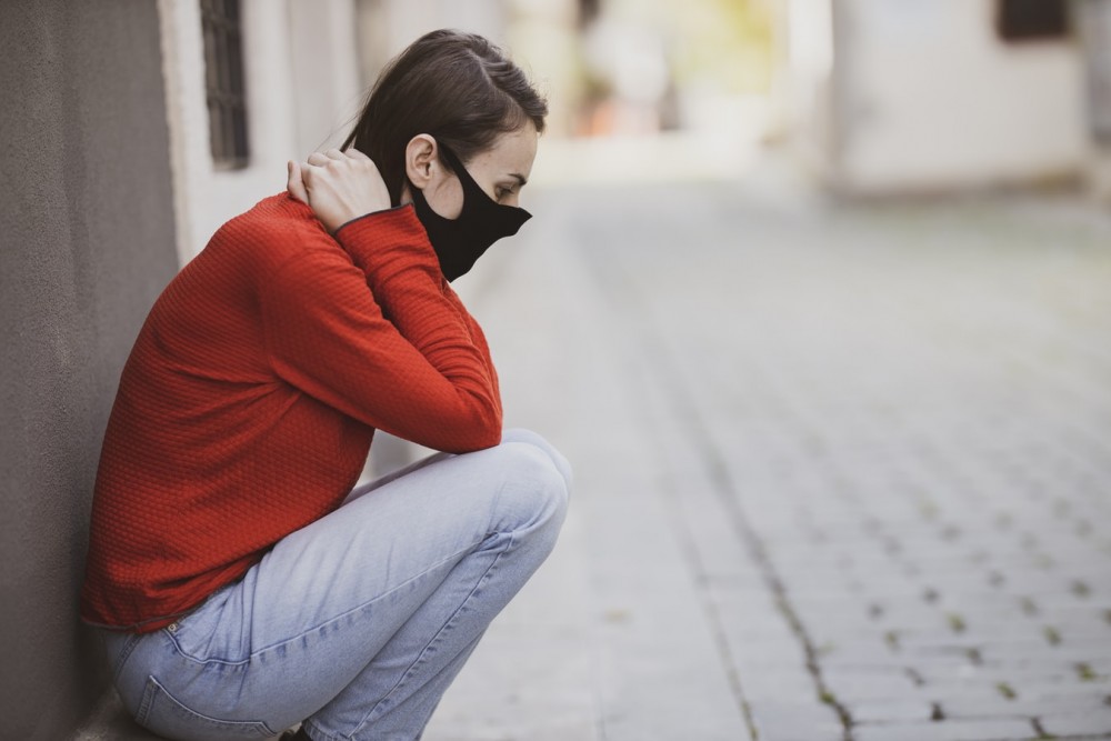 Eine Frau sitzt in der Hocke, die Hände im Nacken verschränkt mit einer Mund-Nasen-Maske.