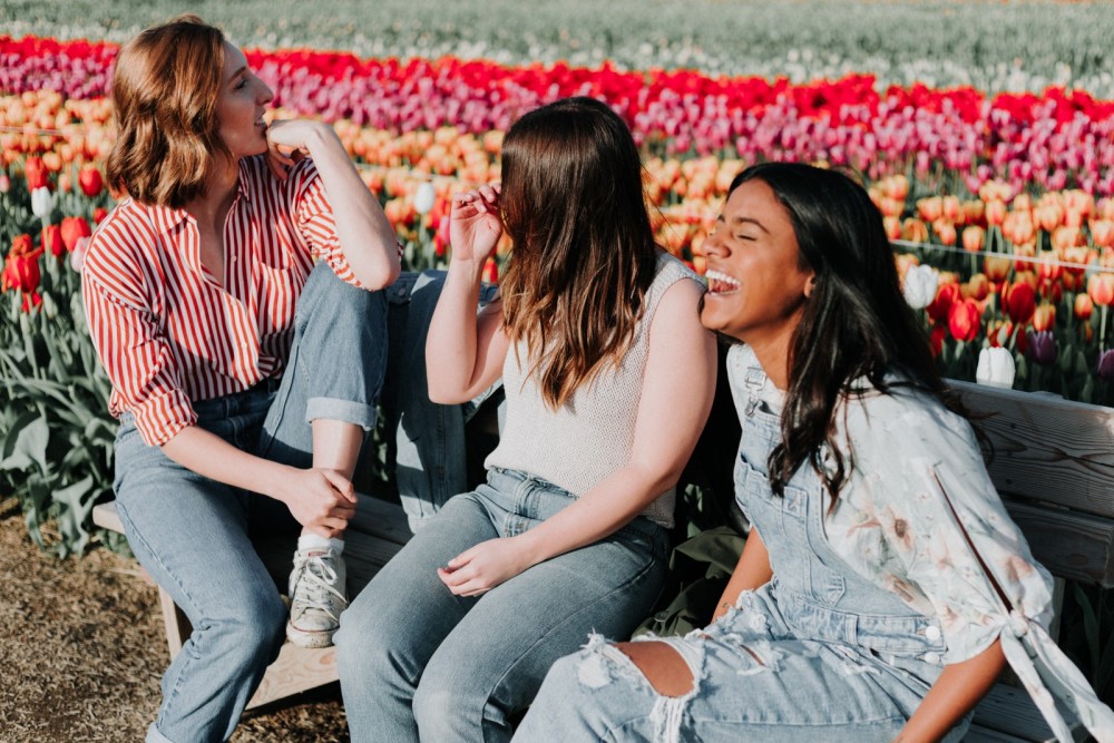 Drei Frauen sitzen auf einer Bank und lachen. 